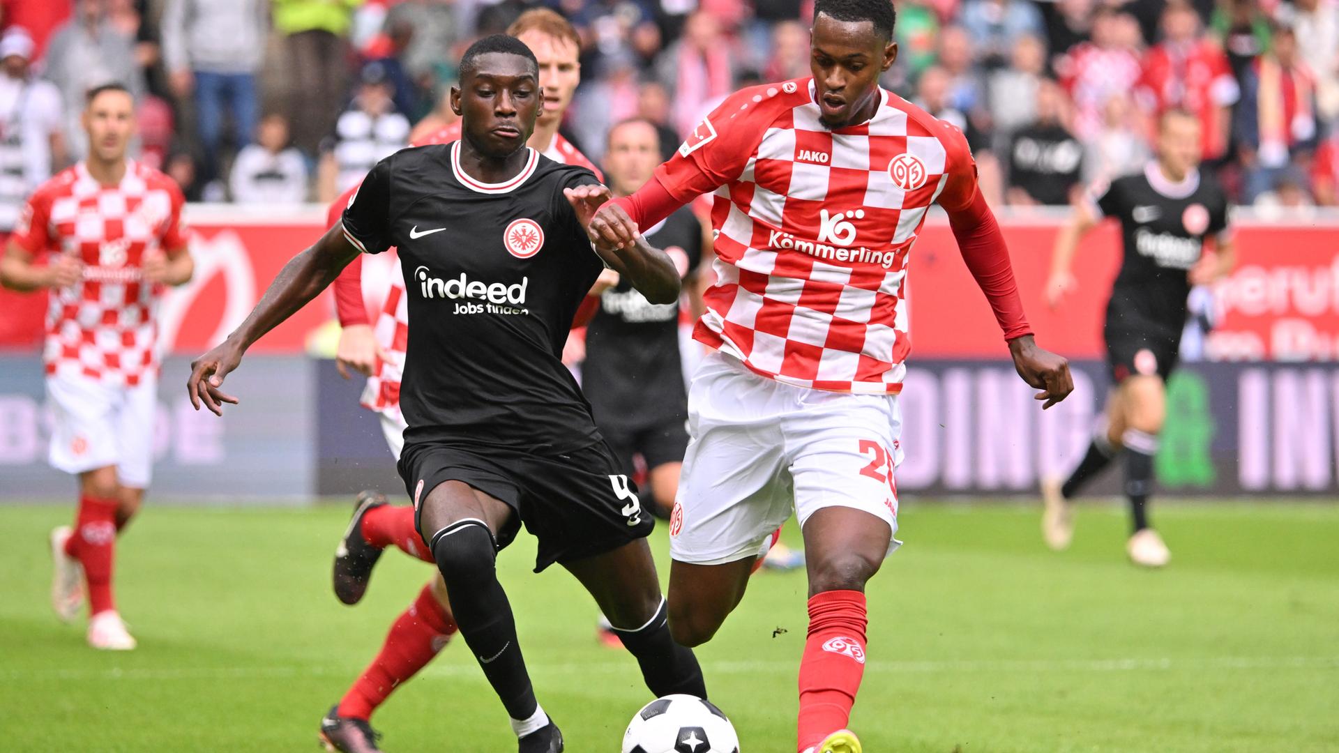 Zu sehen ist Frankfurts Randal Kolo Muani im Duell mit dem Mainzer Edmilson Fernandes. Beide versuchen gleichzeitig, den Ball zu treffen. Zu sehen ist Frankfurts Randal Kolo Muani im Duell mit dem Mainzer Edmilson Fernandes. Beide versuchen gleichzeitig, den Ball zu treffen.