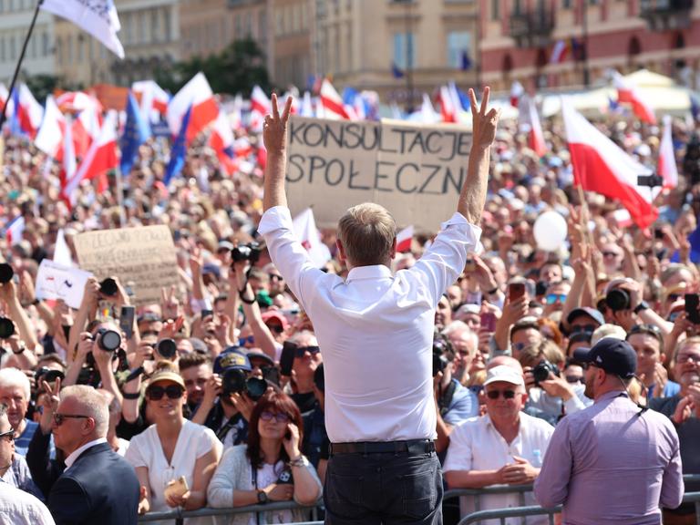 Oppositionspolitiker Donald Tusk steht mit erhobenen Armen in Warschau vor den Teilnehmenden der Großdemonstration gegen die Politik der nationalkonservativen Regierungspartei PiS.