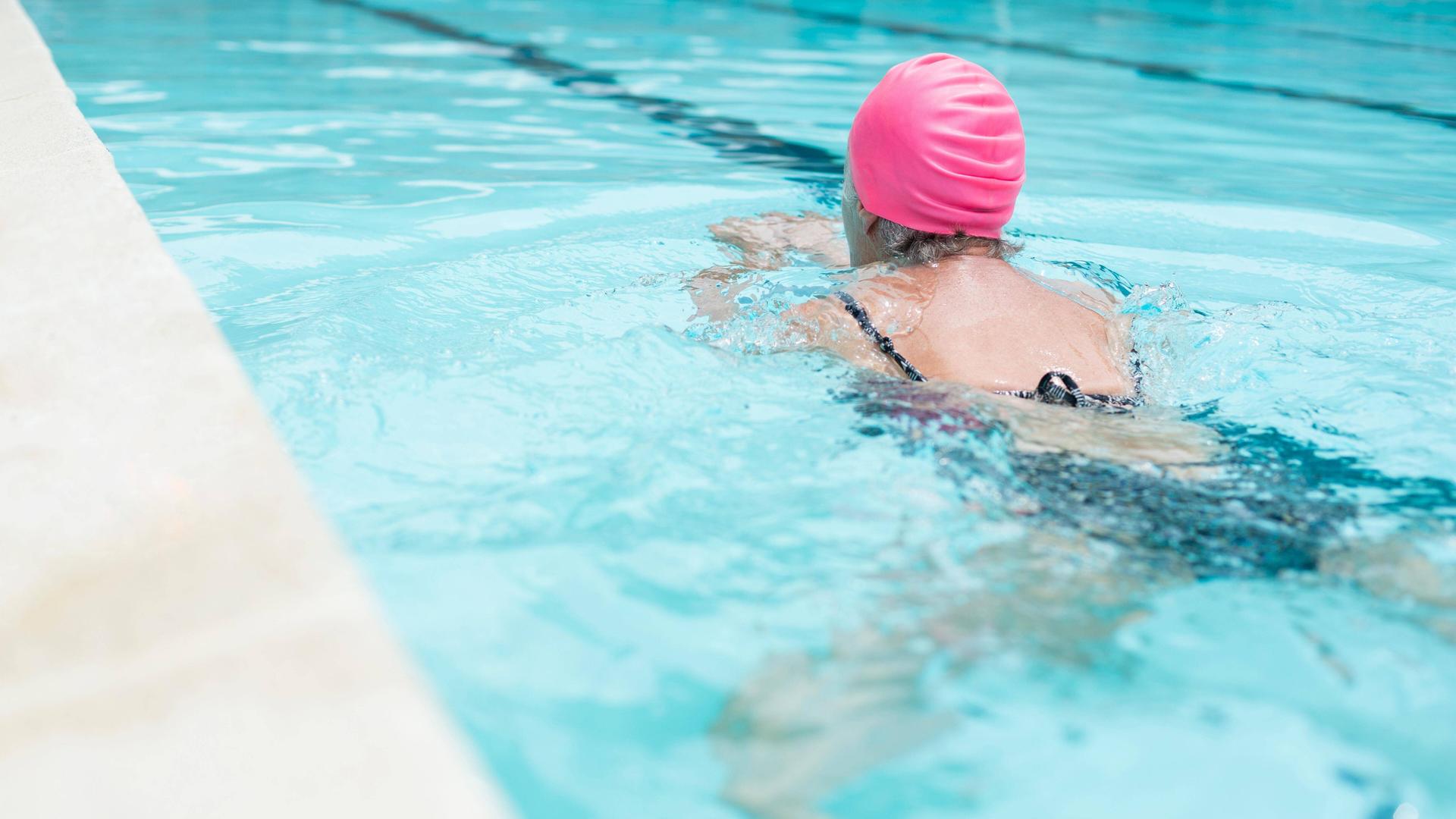 Eine Frau mit einer rosa Badekappe schwimmt in einem Schwimmbecken