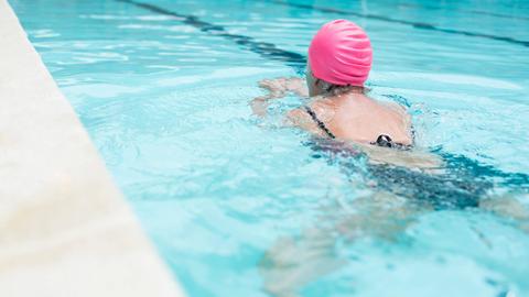 Eine Frau mit einer rosa Badekappe schwimmt in einem Schwimmbecken