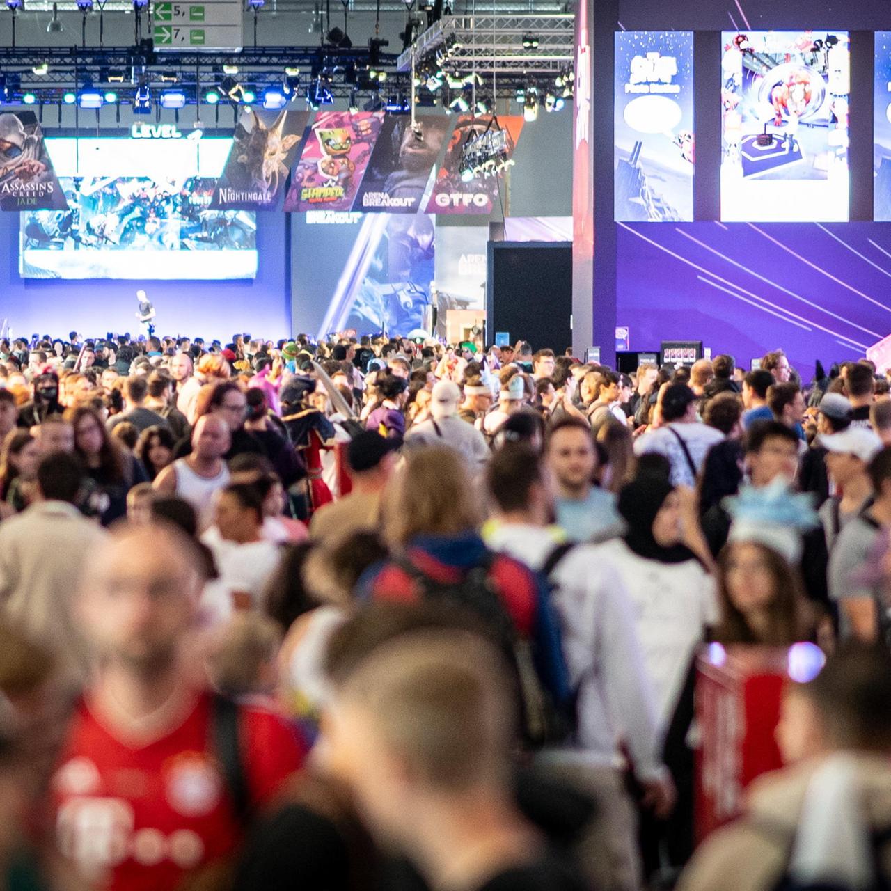 Eine Messe-Halle ist voller Menschen, an der Wand hängen große Plakate von Computer-Spielen.