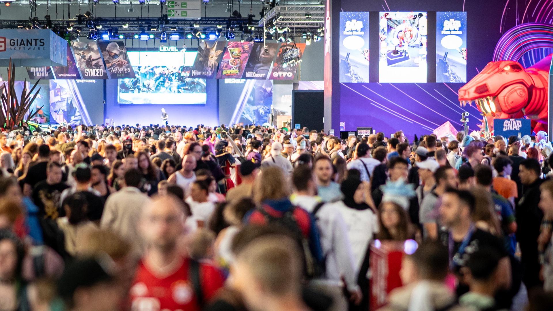 Eine Messe-Halle ist voller Menschen, an der Wand hängen große Plakate von Computer-Spielen.