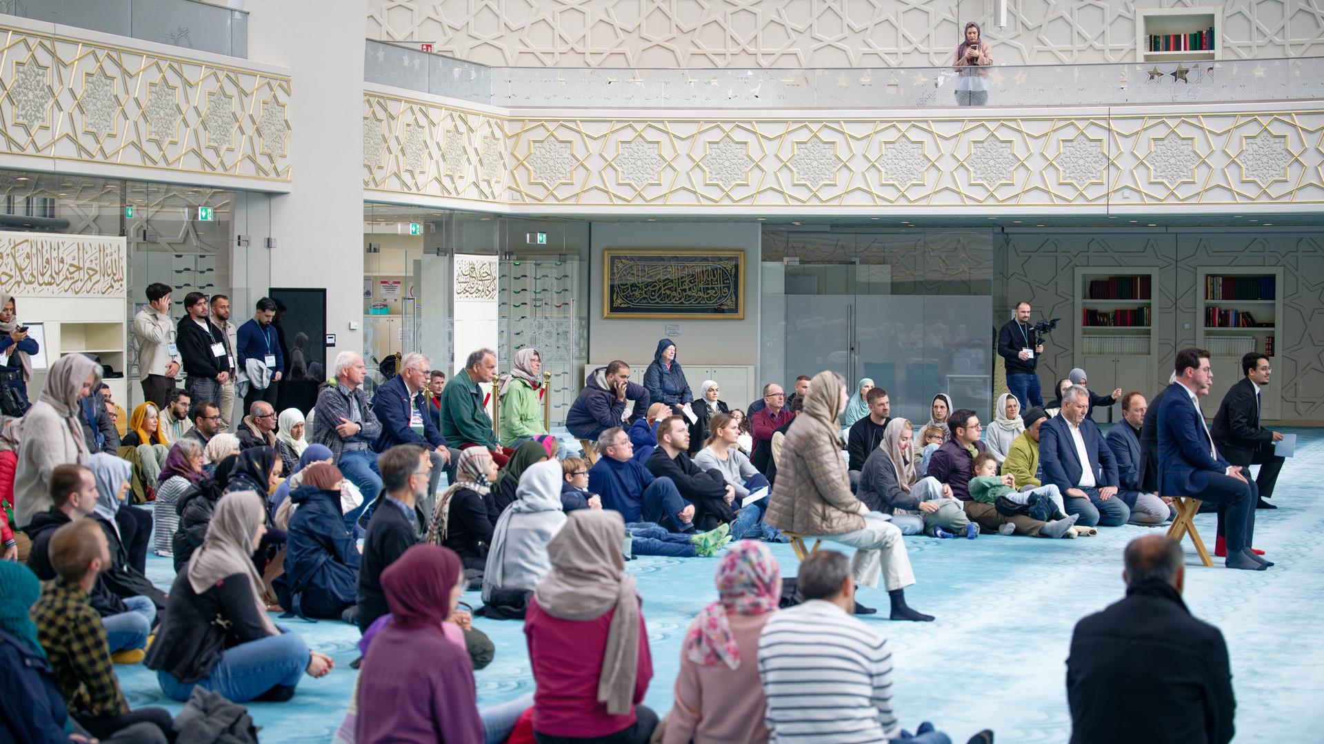 Besucher sitzen auf dem Teppich-Boden der Moschee, die Wände sind reich verziert