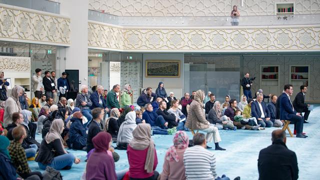 Besucher sitzen auf dem Teppich-Boden der Moschee, die Wände sind reich verziert