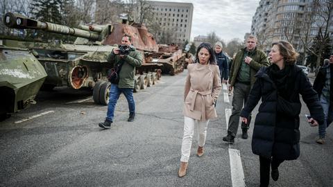 Bundesaußenministerin Annalena Baerbock geht bei ihrem Besuch in Mykolajiw an zerstörten russischen Panzern vorbei. Neben ihr laufen mehrere weitere Menschen.