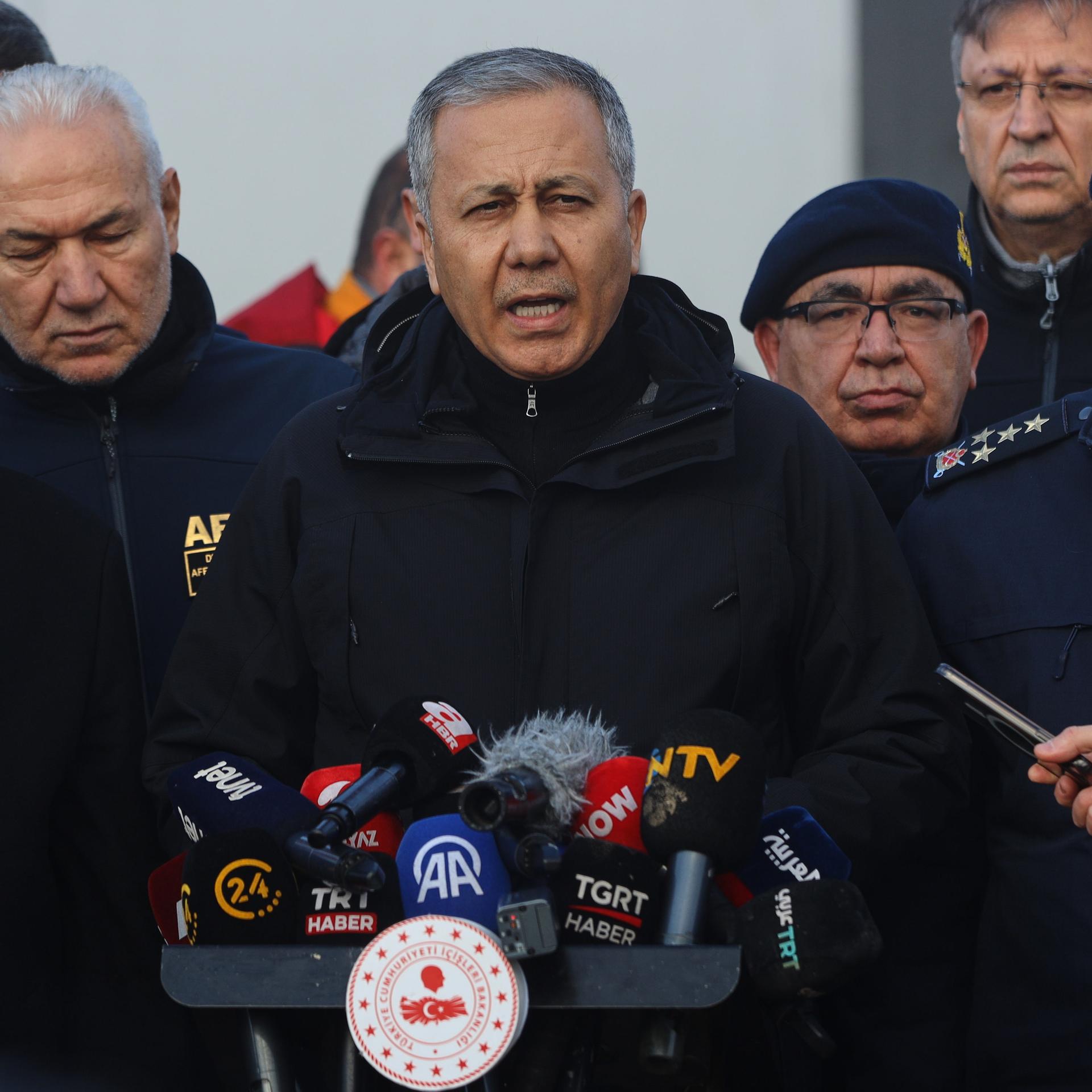 Der türkische Innenminister Ali Yerlikaya (M) spricht zu den Medien. Neben ihm stehen mehrere Personen.  