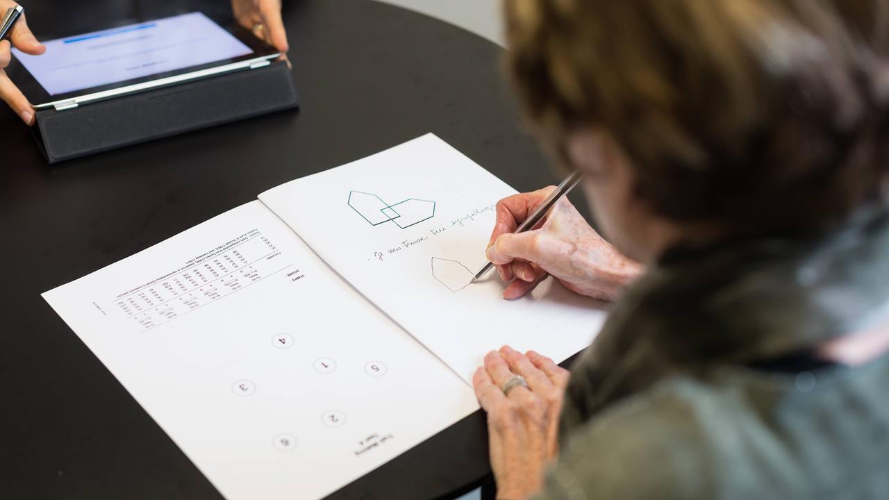 Eine Frau sitzt an einem schwarzen Tisch und füllt einen Testbogen aus. Die Kamera blickt ihr dabei über die Schulter.