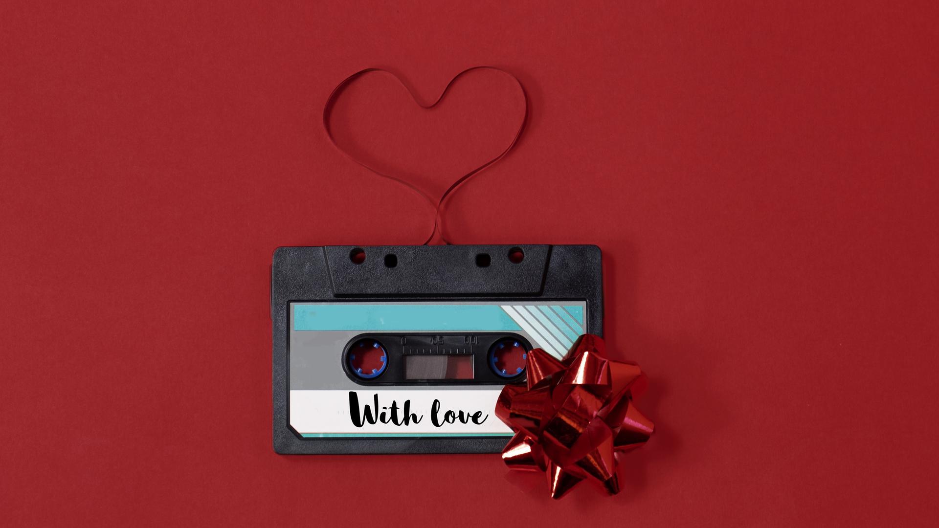 Eine Kassette auf der "With Love" steht und deren Tape zu einem Herz ausgerollt wurde.