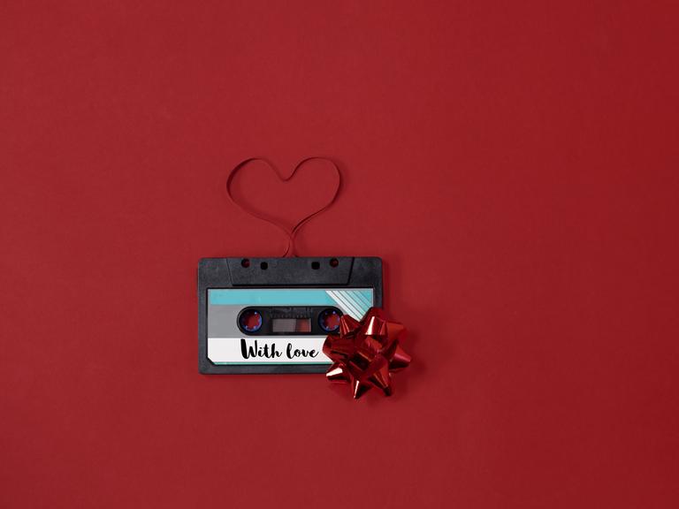 Eine Kassette auf der "With Love" steht und deren Tape zu einem Herz ausgerollt wurde.