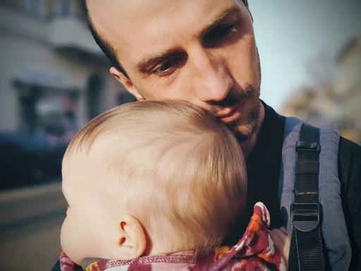 Ein junger Vater mit seinem Sohn im Babyalter. Er legt seine Wange an den Kinderkopf.. 