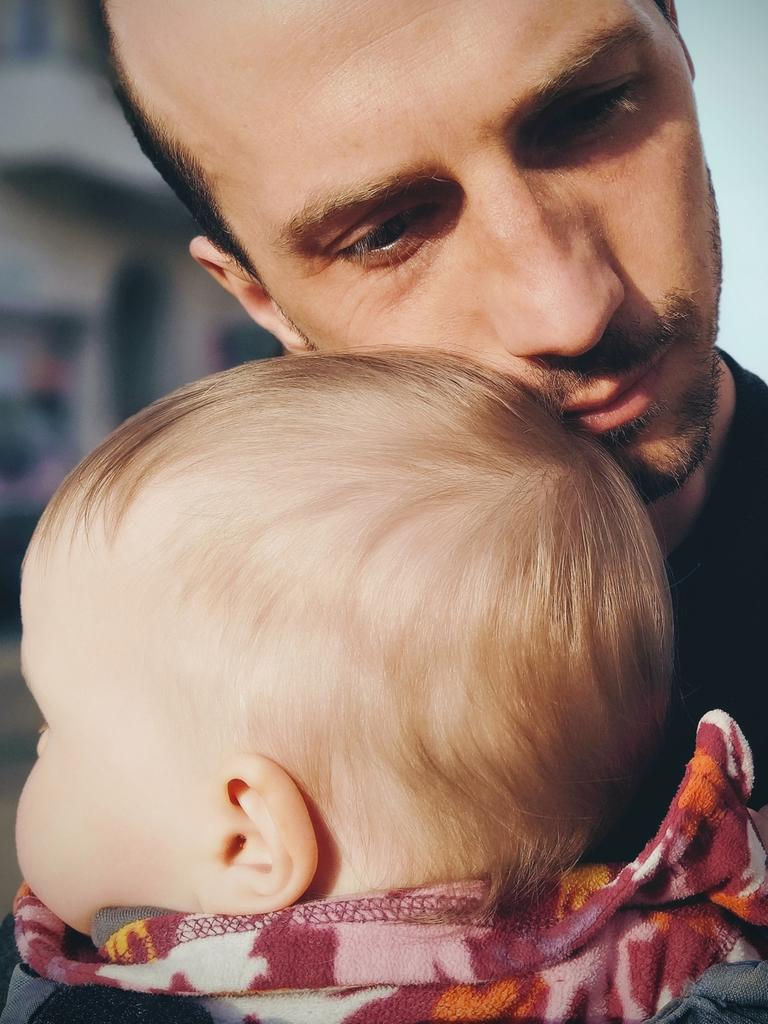 Ein junger Vater mit seinem Sohn im Babyalter. Er legt seine Wange an den Kinderkopf.. 