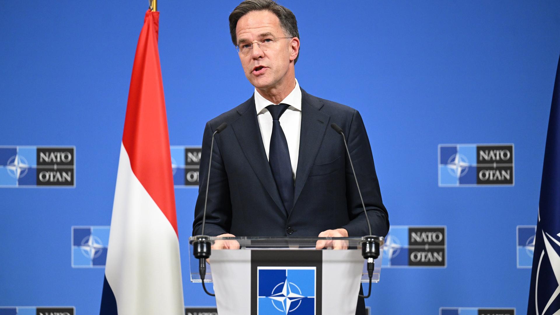 Marc Rutte an einem Rednerpult vor einer Wand mit dem NATO-Logo, neben sich eine niederländische Flagge