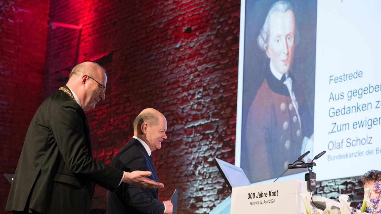 Christoph Markschies, der Präsident der Berlin-Brandenburgischen Akademie der Wissenschaften, weist Bundeskanzler Olaf Scholz den Weg zum Rednerpult; im Hintergrund ist ein Abbild von Immanuel Kant als Projektion zu sehen.