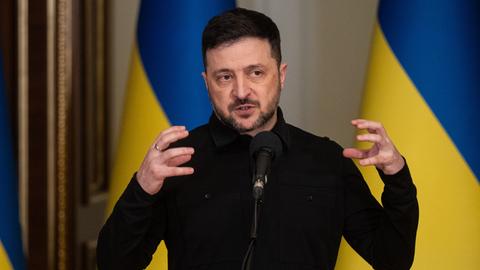 Wolodymyr Selenskyj, Präsident der Ukraine, spricht während eines Briefings. Hinter ihm sind ukrainische Flaggen zu sehen.