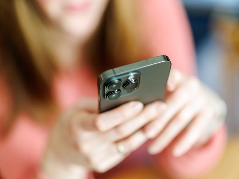 Eine junge Frau benutzt ein Smartphone. Das Bild der Frau ist verschwommen.