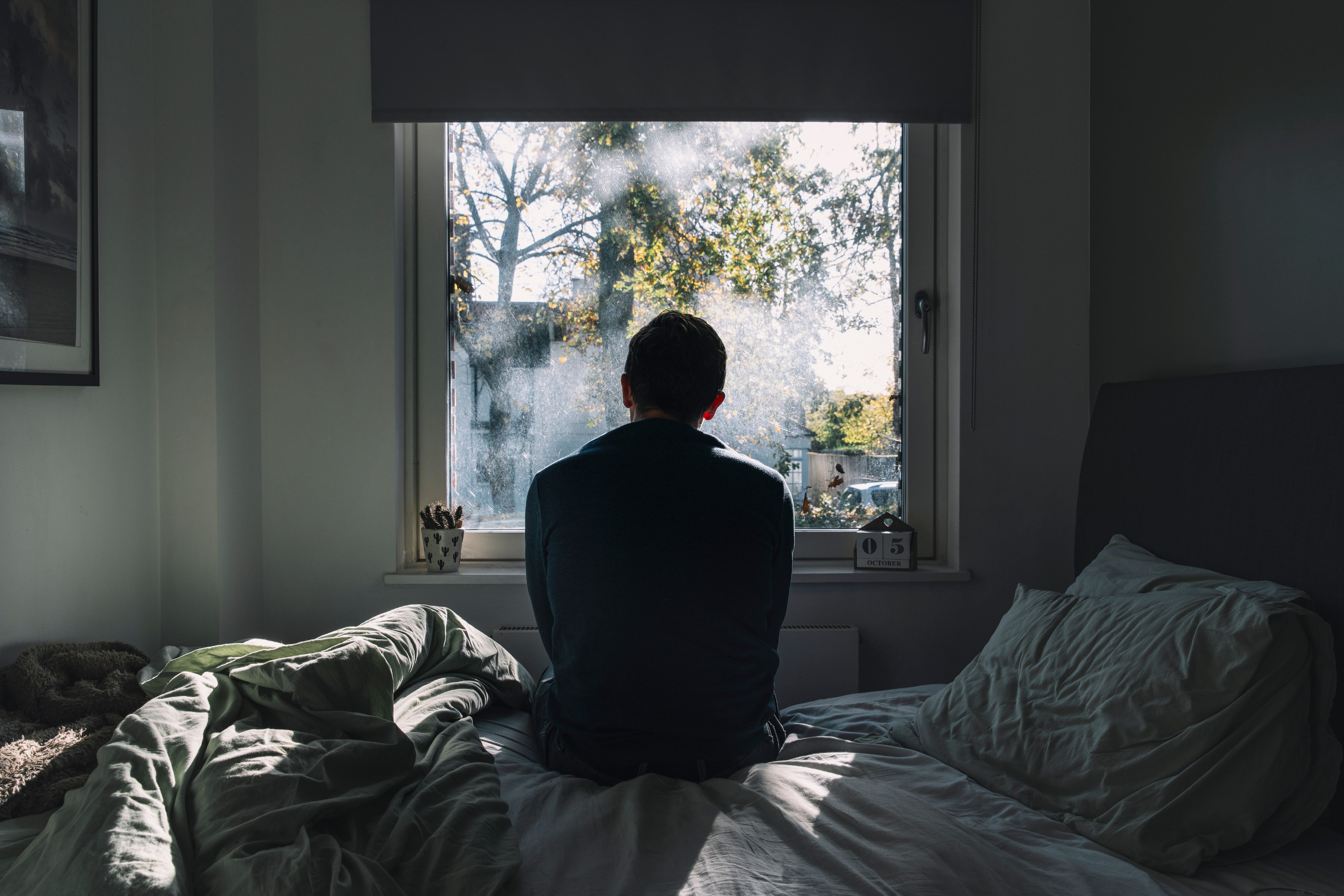 Rückenansicht eines Mannes, der auf einem Bett sitzt und aus dem Fenster schaut