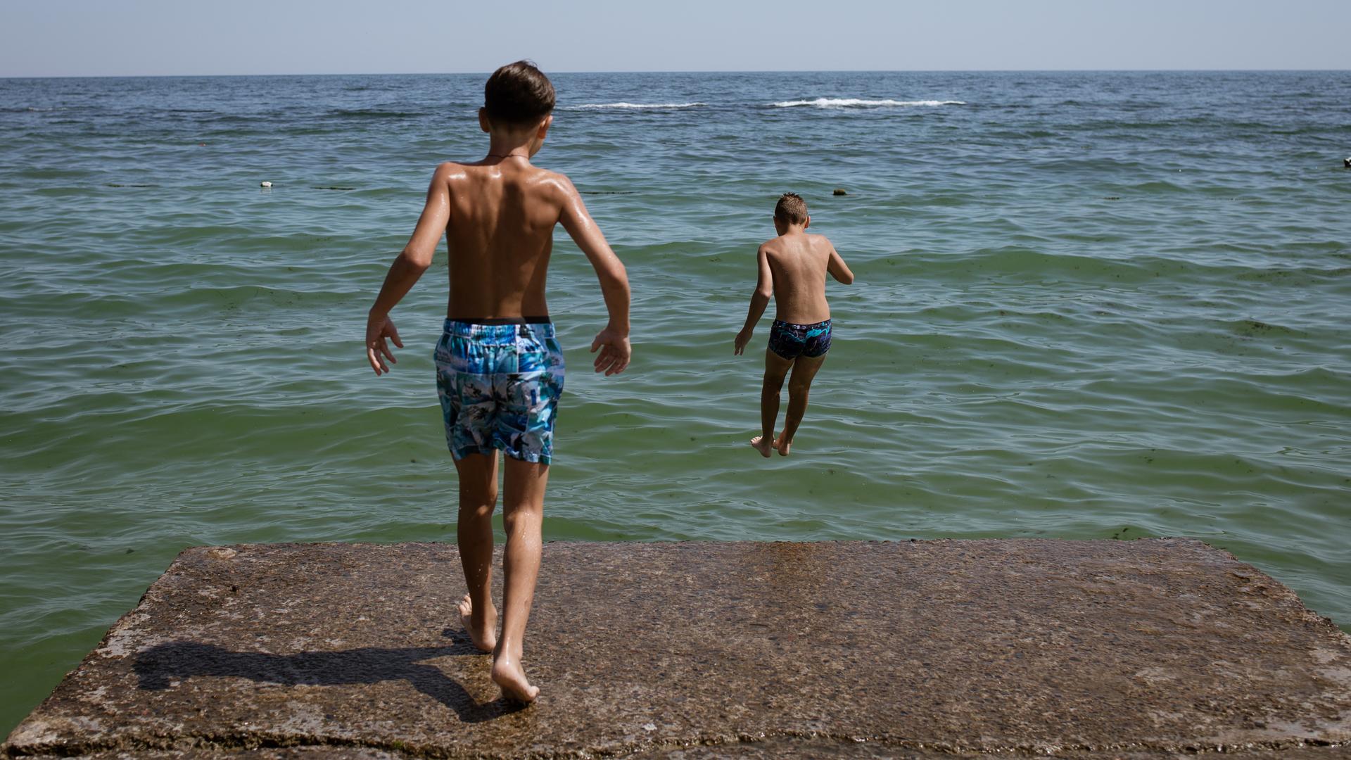 Ein Junge springt in Odessa vom Strand ins Wasser, ein zweiter ist kurz vor dem Sprung. 