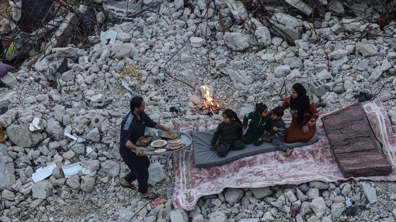 Eine Familie im Gazastreifen hat ein Tuch auf Trümmern ausgebreitet, um dort zu während des Ramadan das Fasten zu brechen. Ein Mann bringt Essen auf einem Tablett für eine Frau und Kinder.