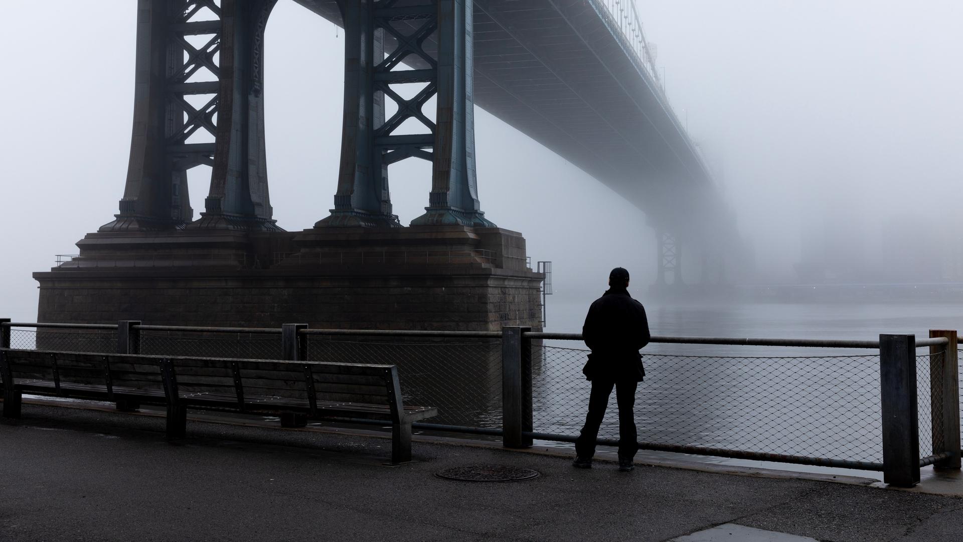 Eine Person steht im dichten Nebel unter der Manhattan Bridge. (Symbolbild)