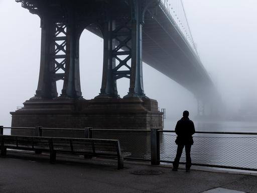 Eine Person steht im dichten Nebel unter der Manhattan Bridge. (Symbolbild)