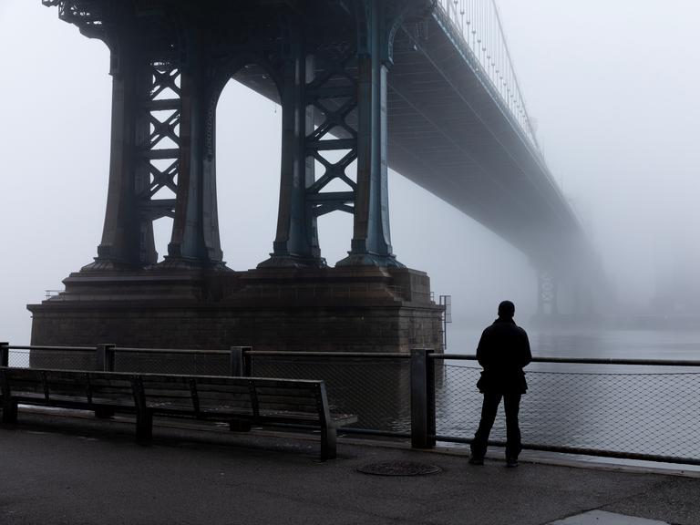 Eine Person steht im dichten Nebel unter der Manhattan Bridge. (Symbolbild)