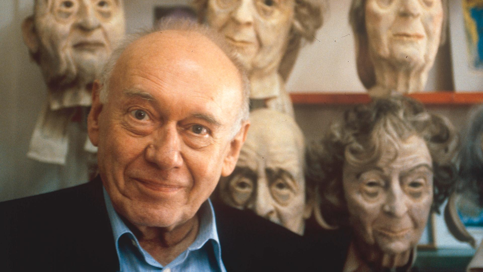 Der Schriftsteller Ernst Jandl 1995, hinter ihm grotesk wirkende Gesichtsmasken.