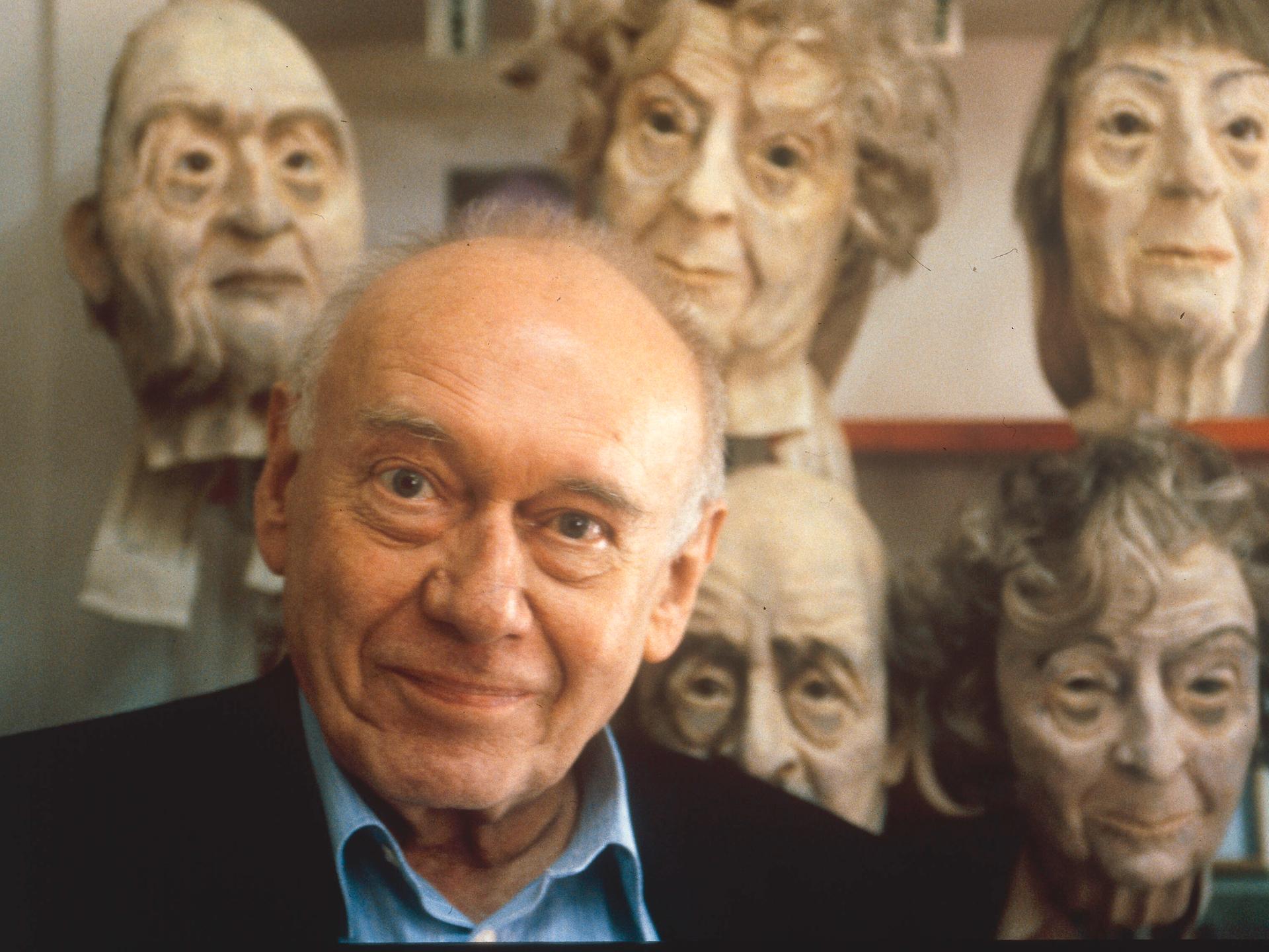 Der Schriftsteller Ernst Jandl 1995, hinter ihm grotesk wirkende Gesichtsmasken.