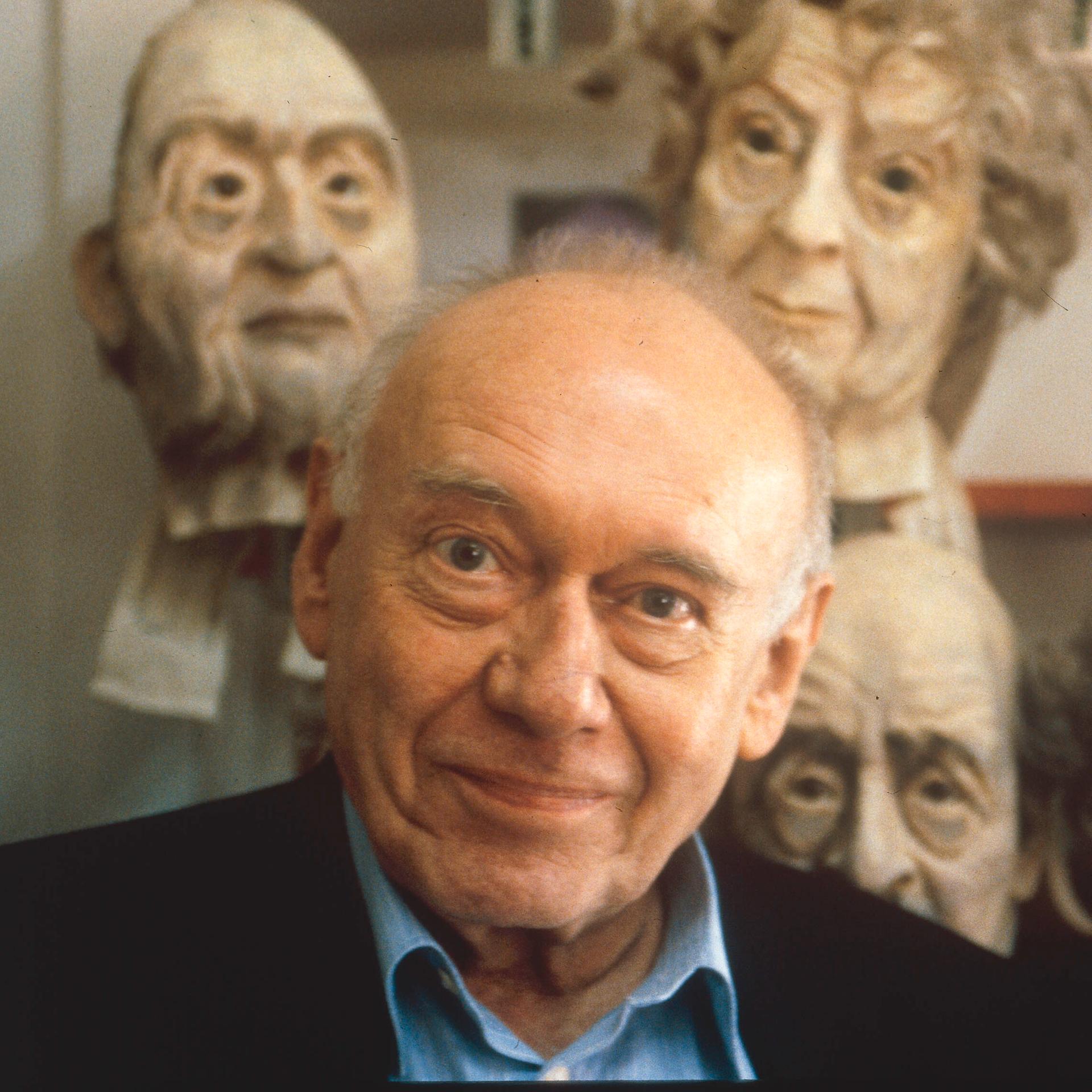 Der Schriftsteller Ernst Jandl, hinter ihm die Köpfe von grotesken Puppen.