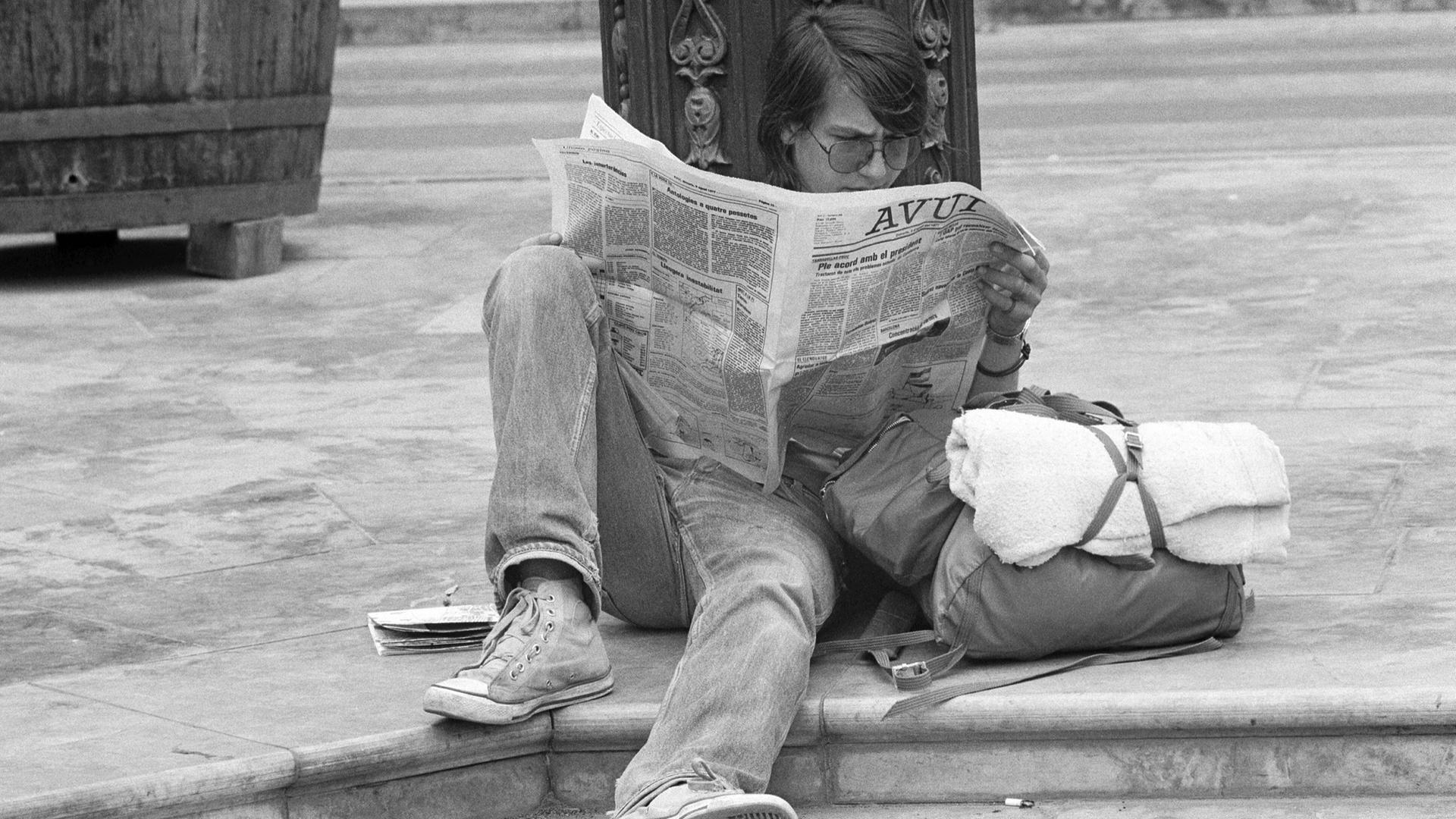 Ein Schwarz-Weiß-Foto zeigt einen Jugendlichen, der im Jahr 1977 in Valencia in Spanien am Straßenrand auf dem Boden sitzt und eine Zeitung liest. Ein Schwarz-Weiß-Foto zeigt einen Jugendlichen, der im Jahr 1977 in Valencia in Spanien am Straßenrand auf dem Boden sitzt und eine Zeitung liest.