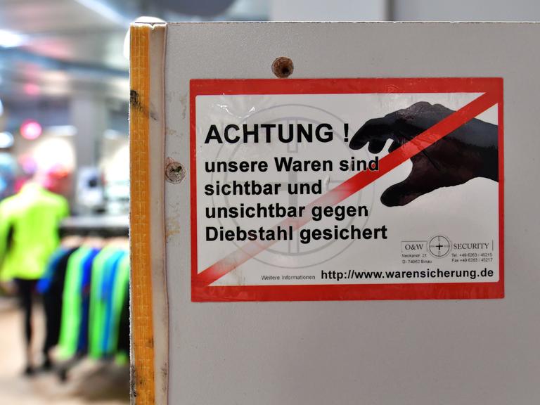 Ein Aufkleber mit der Aufschrift "Achtung ! unsere Waren sind sichtbar und unsichtbar gegen Diebstahl gesichert" an der Umkleidekabine in einem Sportgeschäft