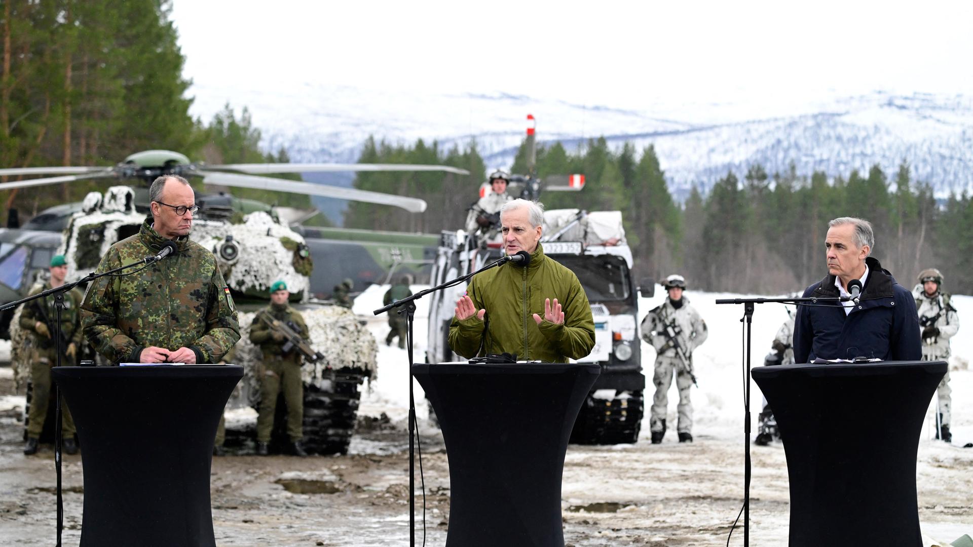 Bundeskanzler Merz bei einer gemeinsamen Pressekonferenz mit den Regierungschefs von Norwegen und Kanada, Jonas Gahr Støre und Mark Carney im norwegischen Bardufoss . Im Hintergrund sieht man einen Hubschrauber und Fahrzeuge der Armee.