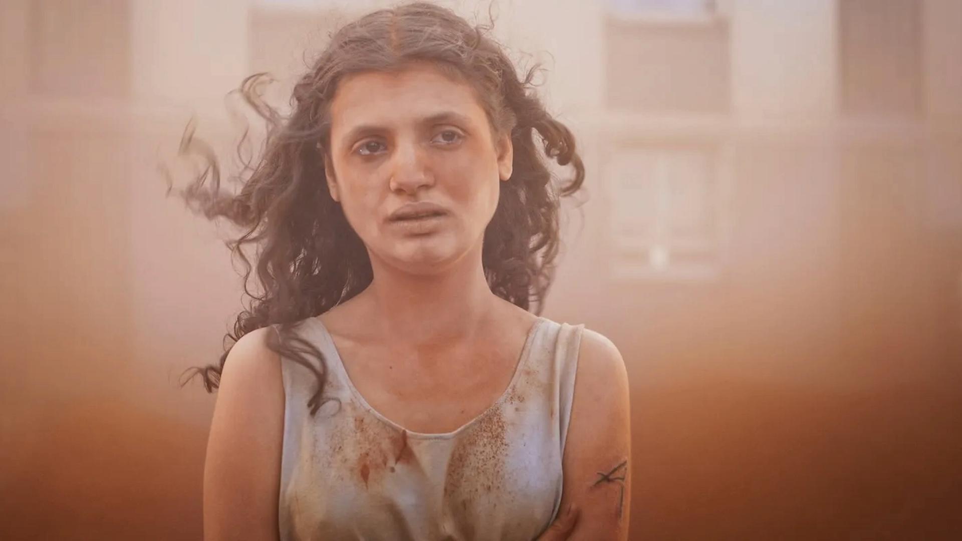 Im Still aus "Alpha" steht eine junge Frau mit langen dunklen Locken in einem Sandsturm. Sie hat einen erschöpften Gesichtsausdruck. Im Still aus "Alpha" steht eine junge Frau mit langen dunklen Locken in einem Sandsturm. Sie hat einen erschöpften Gesichtsausdruck.