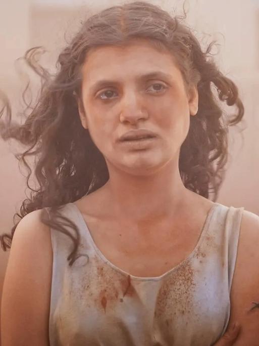 Im Still aus "Alpha" steht eine junge Frau mit langen dunklen Locken in einem Sandsturm. Sie hat einen erschöpften Gesichtsausdruck.