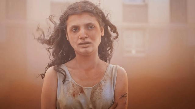 Im Still aus "Alpha" steht eine junge Frau mit langen dunklen Locken in einem Sandsturm. Sie hat einen erschöpften Gesichtsausdruck.