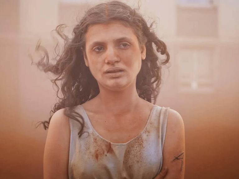 Im Still aus "Alpha" steht eine junge Frau mit langen dunklen Locken in einem Sandsturm. Sie hat einen erschöpften Gesichtsausdruck.
