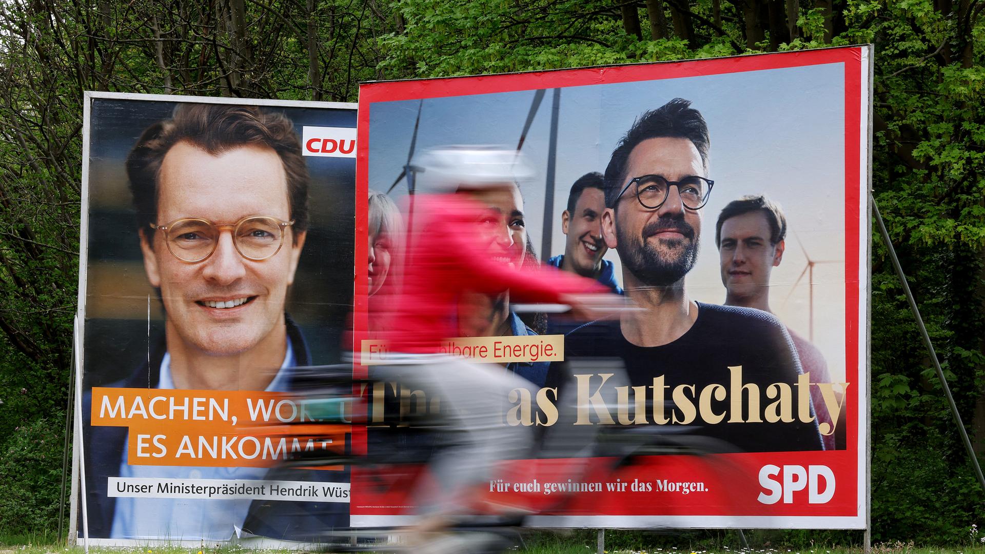 Wahlplakate mit Portraits der nordrhein-westfälischen Spitzenkandidaten von CDU, Ministerpräsident Hendrik Wüst (l), und SPD, Thomas Kutschaty (r), stehen auf einer Wiese. In Nordrhein-Westfalen findet am 15. Mai 2022 die Landtagswahl statt.