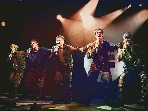 Take That stehen auf einer Bühne und führen eine Tanzchoreografie auf