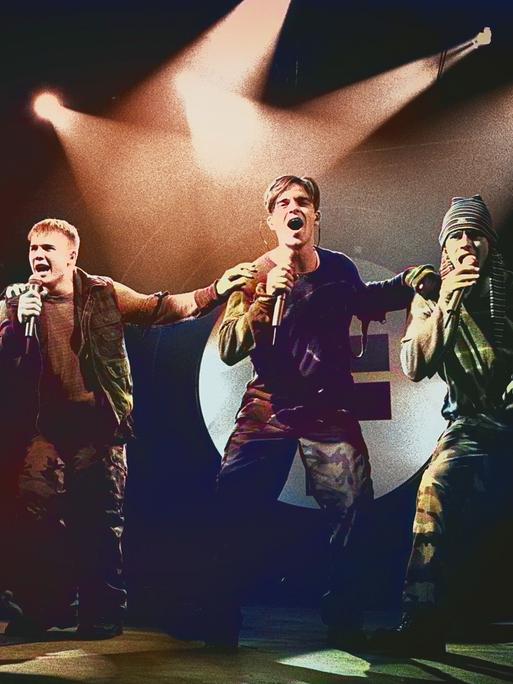 Take That stehen auf einer Bühne und führen eine Tanzchoreografie auf