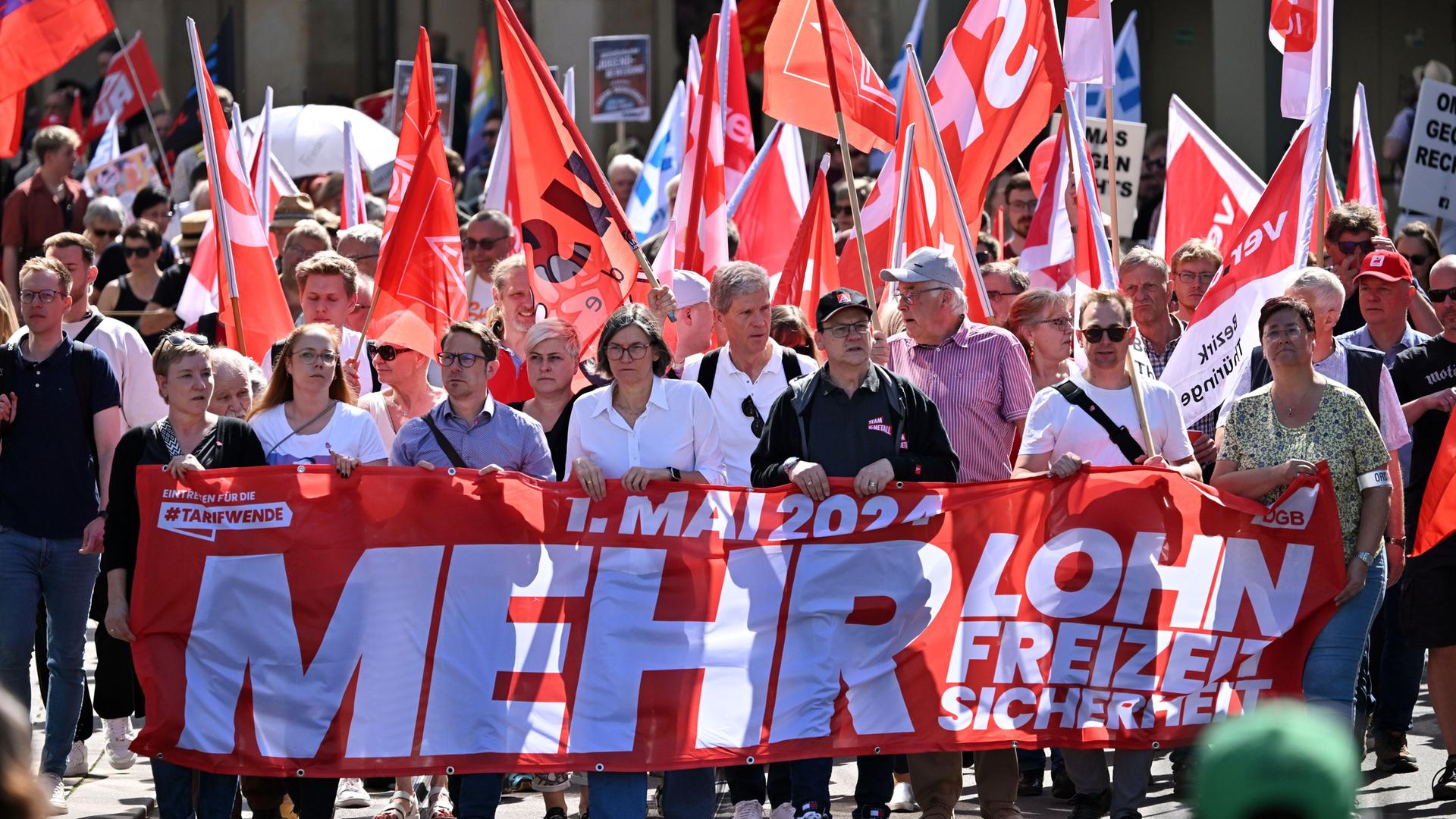 Menschen laufen in Erfurt gemeinsam durch die Straße. Sie halten rote Fahnen und ein rotes Schild. Darauf steht "Mehr Lohn". 