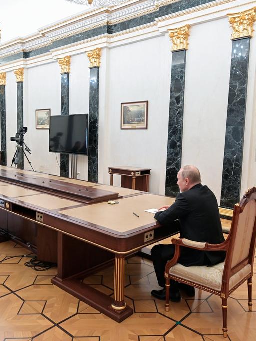 Wladimir Putin sitzt an einem überlangen Tisch im Gespräch mit seinem Verteidigungsminister und einem General der Streitkräfte. 