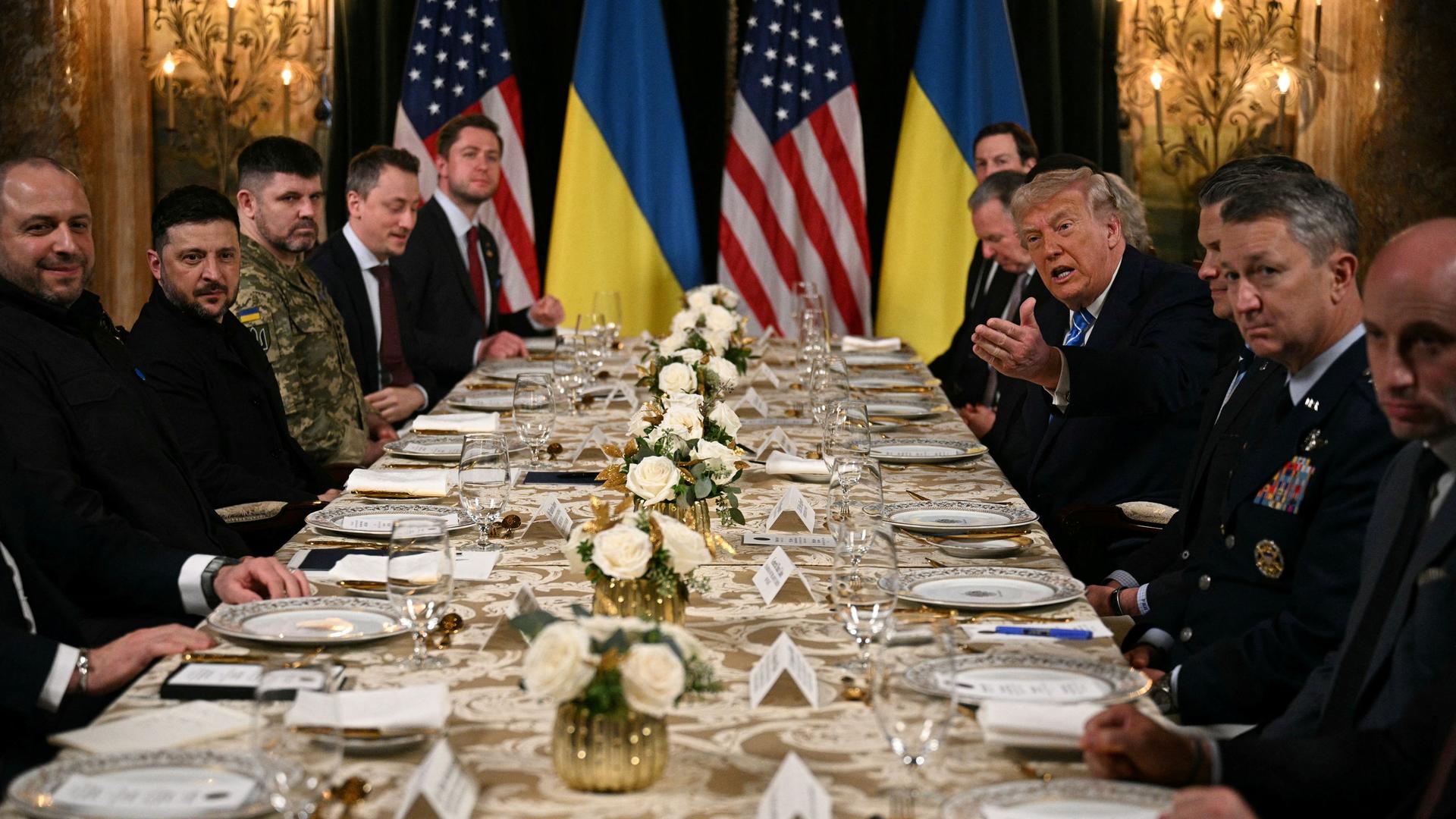 US-Präsident Trump empfängt den ukrainischen Präsidenten Selenskyj in Mar-a-Lago. Zusammen mit ihren Delegationen sitzen sie an einem langen Tisch.