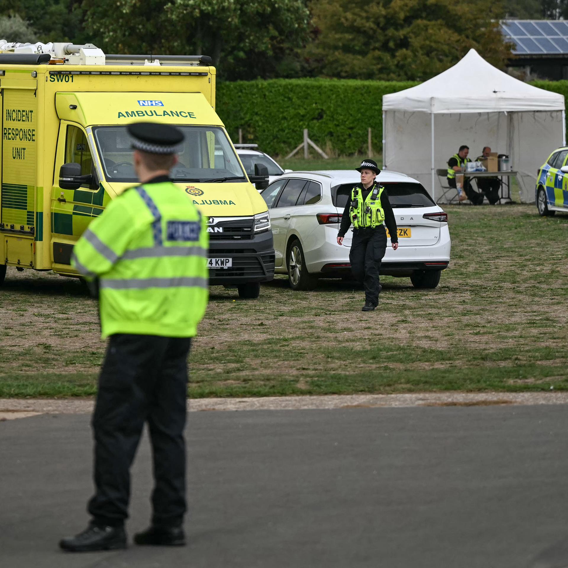 Mehrere Polizeifahrzeuge und ein Pavillion auf einer Wiese, dazwischen laufen und sitzen mehrere Polizistinnen und Polizisten.
