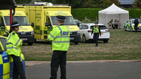Mehrere Polizeifahrzeuge und ein Pavillion auf einer Wiese, dazwischen laufen und sitzen mehrere Polizistinnen und Polizisten.