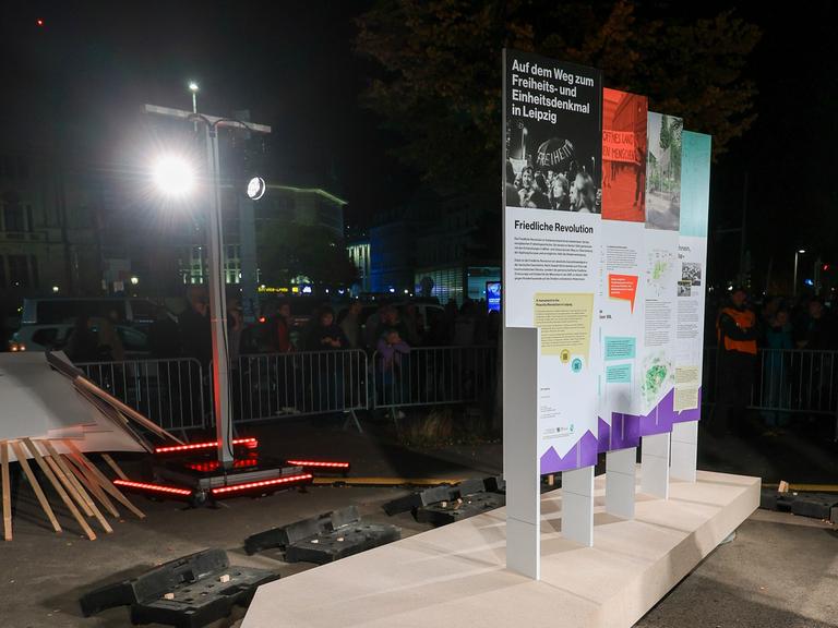 Der Grundstein für das Freiheits- und Einheitsdenkmals wird während des Lichtfestes in der Leipziger Innenstadt enthüllt. Am Boden liegt ein Betonplatte, darauf befestigt sind 4 Aufsteller mit Schrift und Bildern.