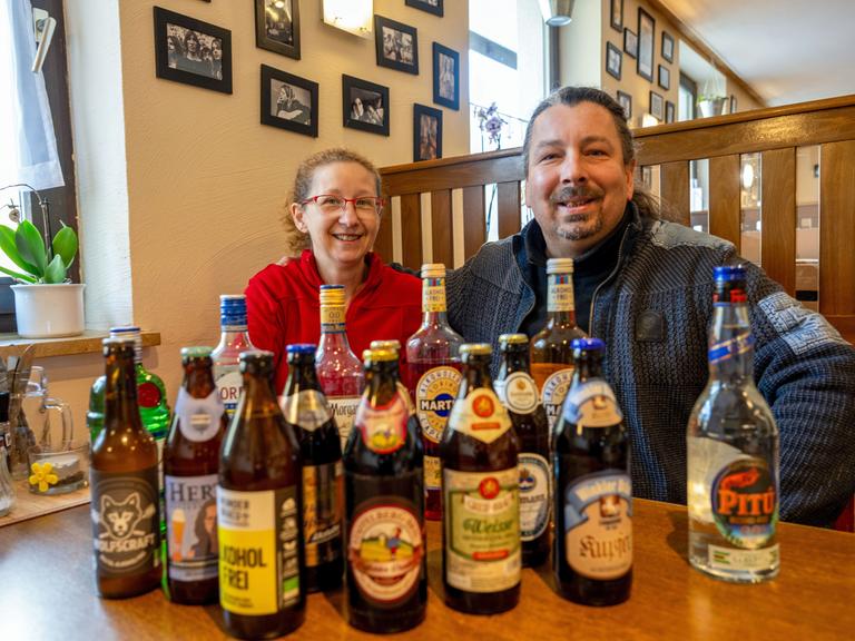 Kerstin Gößl und Vladimir Kloz sitzen hinter zahlreichen Flaschen alkoholfreier Biere und weiterer alkoholfreier Getränke