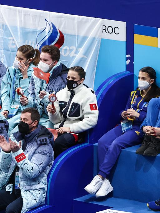 Russische und ukrainische Sportlerinnen und Sportler sitzen beim Eiskunstlaufwettkampf in Peking direkt nebeneinander.  