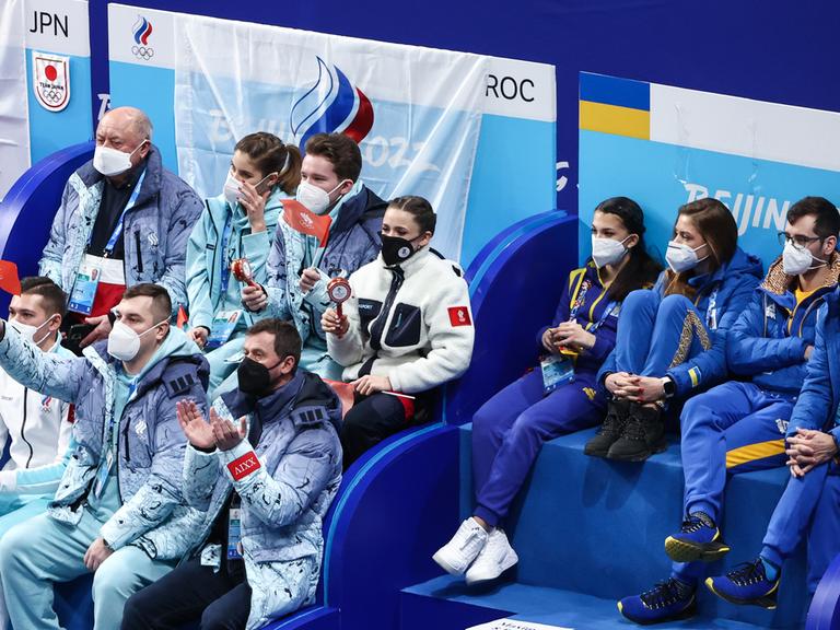 Russische und ukrainische Sportlerinnen und Sportler sitzen beim Eiskunstlaufwettkampf in Peking direkt nebeneinander.  