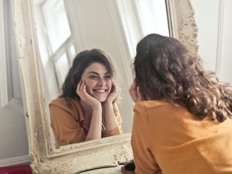 Eine junge Frau lächelt ihr Spiegelbild an