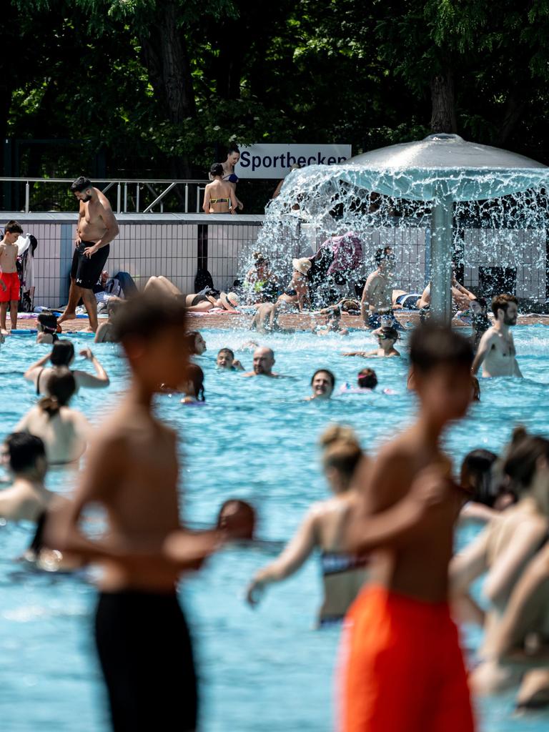Viele Menschen baden im Freibad oder sitzen um das große Schwimmbecken herum.