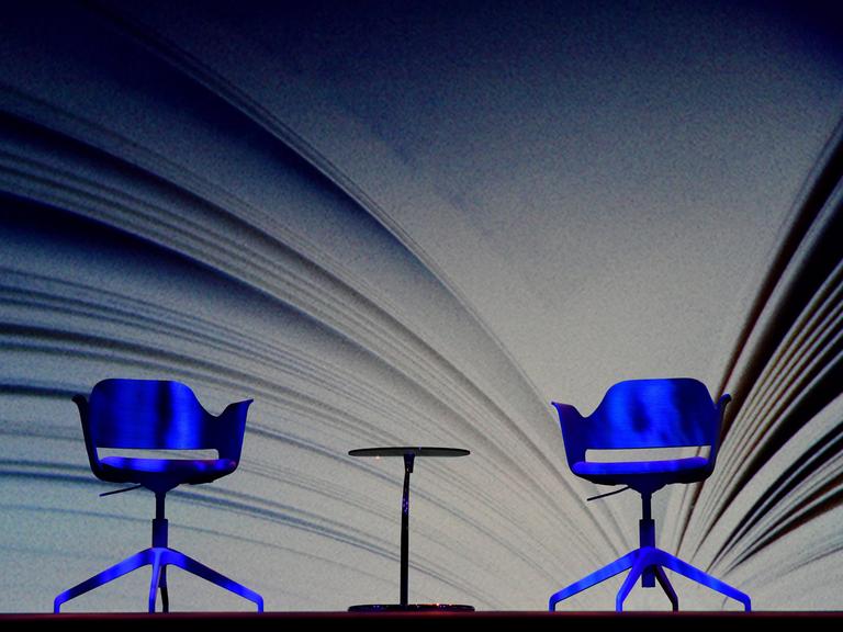 Zwei leere Stühle und ein Tisch stehen vor einer riesigen Buchprojektion auf der Frankfurter Buchmesse.